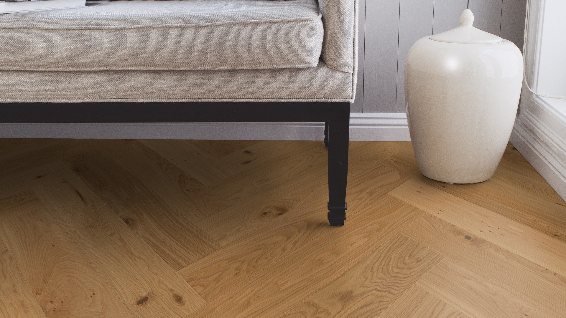 Kalanruotoparketti Tammi Mix 140 mm, 4 sivulta viistetty, harjattu, Osmo öljyvahaa – asennettu eteisen lattialle. Beigenvärinen sohva mustilla jaloilla, valkoiseksi maalatut jalkalistat, harmaat seinäpaneelit, valkoinen roskakori.