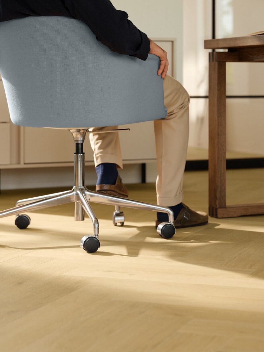 laminat-quick-step-impressive-design-nutmeg-oak Laminat Quick Step Impressive Suunnittelu Nutmeg Oak, verlegt im Büro, blauer Bürostuhl mit sitzendem Mann