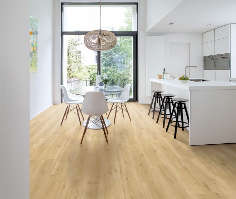 lvt-porandakate-quick-step-blos-drift-tamm-beige LVT põrandakate Quick-Step Blos Drift tamm beige paigaldatud köögi põrandale. Valge köögimööbel, köögisaar koos musta värvi toolidega. Ümar söögilaud koos valgete toolidega.