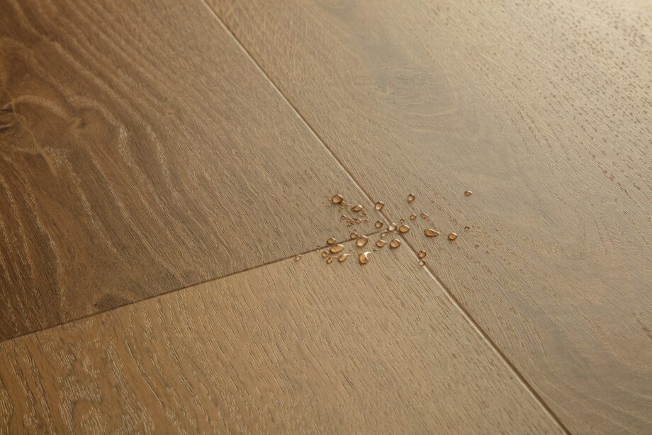 vinyylilankku-quick-step-bloom-elegant-fumed-oak Vinyylilankku Quick Step Bloom Elegant Fumed Oak, tumma savutammen sävy ja lankkudesign, pinnalla vesipisaroita korostamassa lattian vedenkestävyyttä.
