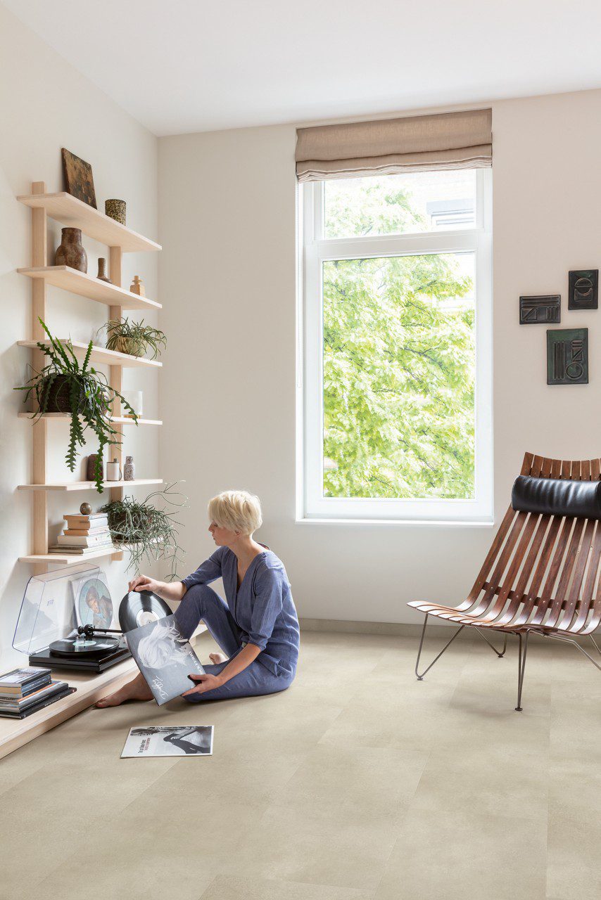 LVT Quick-Step Illume Sandstone concrete betooni disainiga paigaldatud elutoa põrandale. Naisterahvas paneb vinüülplaati vinüülplaadi mämgijasse.