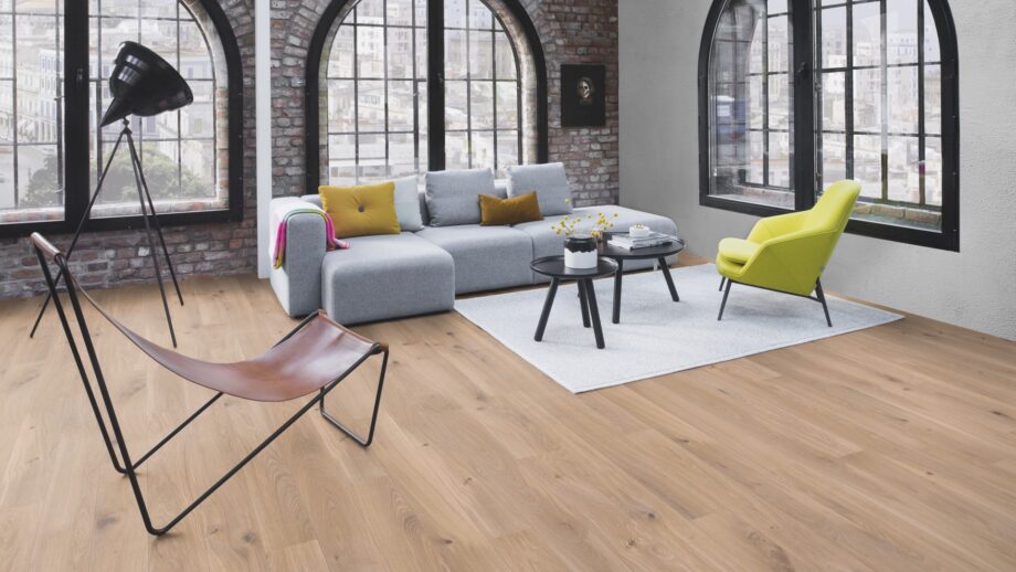 parkett-bauwerk-boen-casapark-eiche-46-gebuerstet-farina-weiss-geoelt Parkett Bauwerk Boen Casapark Eiche 46 Farina, gebürstet und weiß geölt – verlegt auf dem Wohnzimmerboden; graues Sofa, leuchtend grüner Sessel und ein grauer Teppich mit zwei kleinen runden Couchtischen. Rustikale Sortierung mit lebendiger Maserung und Astanteilen.