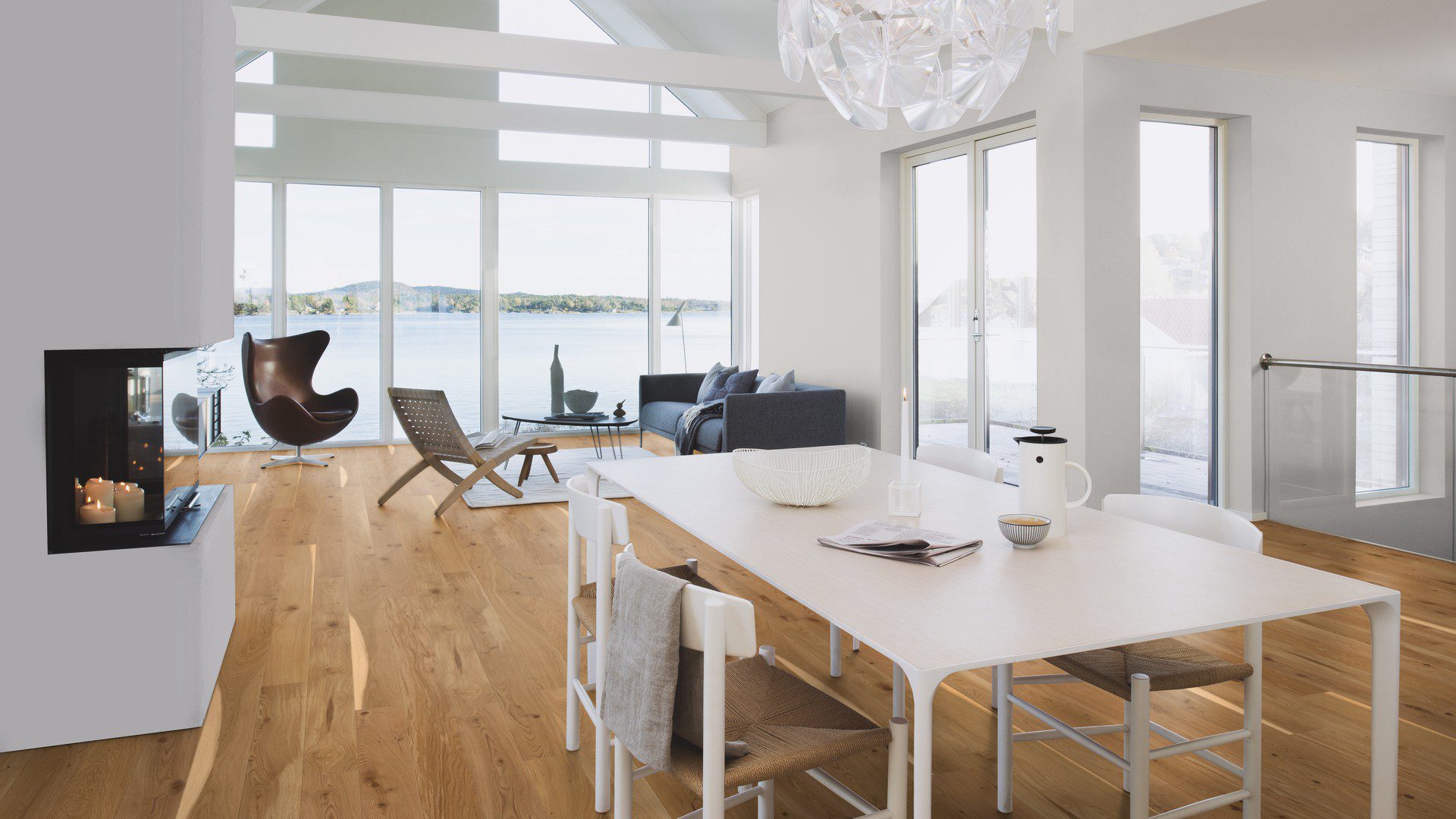 Tammeparkett Bauwerk Boen Casapark tamm 46 Vivo harjatud õlivaha. Paigaldatud avatud köögiga elutoa põrandale. Diivan, tugitool, diivanilaud. Kamin mille sees põlevad küünlad, söögilaud koos toolidega.