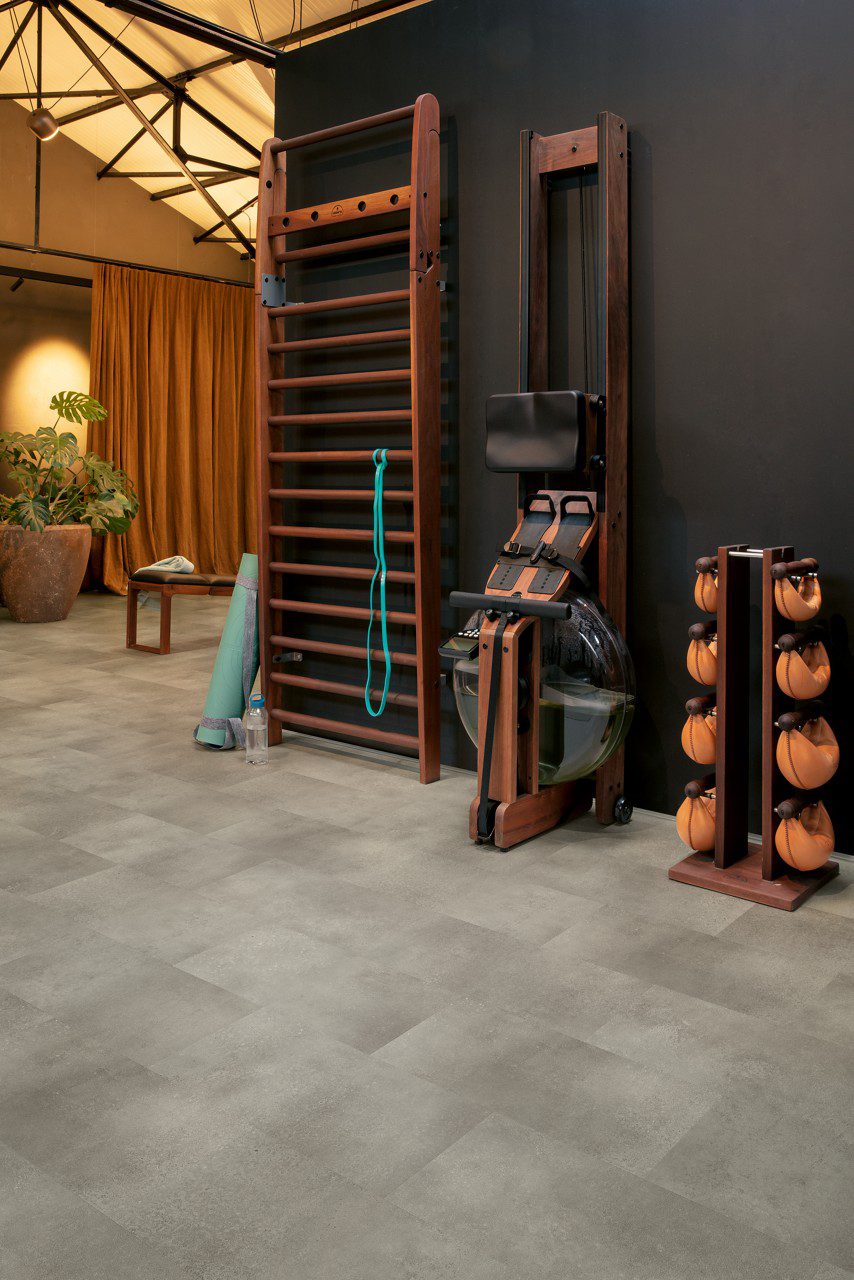 Vinyl floor tiles Quick-Step Oro Concrete rock installed on a home Jim floor. Ladder on wall, yoga mat.