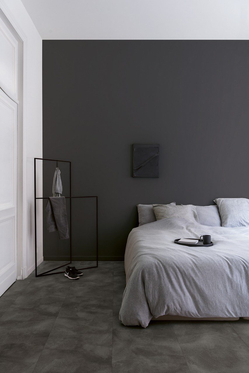Vinyl flooring tiles Quick-Step Illume Soft graphite with dark grey color installed on bedroom floor. King size bed.