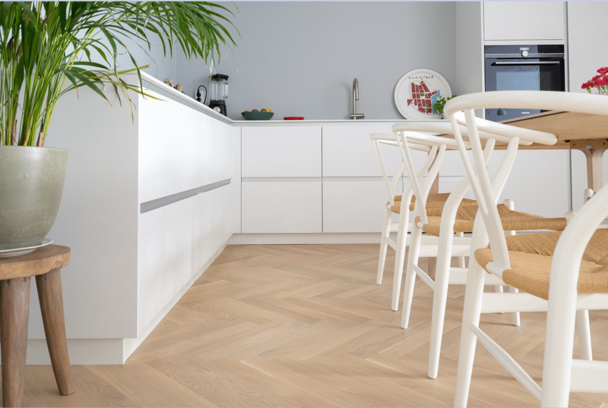Kalanruotoparketti Bauwerk Monopark Tammi 45 Crema b-protect mattalakattu asennettu keittiön lattialle. Valkoiset keittiökalusteet, ruokapöytä, tuolit.