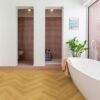 Herringbone laminate floor Quick Step Impressive Suunnittelu Cumin Oak, installed on bathroom floor with a white bathtub