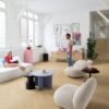klick-vinyl-fisgrät-quick-step-ciro-pure-oak-blush Klick Vinyl Fischgrat Quick Step Ciro Pure Oak Blush, verlegt auf dem Wohnzimmerboden und auf der Treppe mit farblich passender Incizo-Leiste. Eine Frau liegt auf einem weißen Sofa und unterhält sich mit einem Mann, der auf dem Boden steht.