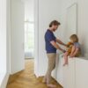 laminat-fischgrat-quick-step-impressive-design-cinnamon-oak Vinylboden Fischgrät Quick Step Impressive Suunnittelu Cinnamon Oak, verlegt im Badezimmerboden, Vater lässt Wasser aus dem Hahn laufen und das Kind sitzt auf der Badezimmermöbelplatte