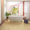 laminat-fischgrat-quick-step-impressive-design-ginger-oak Laminat Fischgrät Quick Step Impressive Suunnittelu Ginger Oak, verlegt im Badezimmerboden, freistehende weiße Badewanne, mit blauer Mosaikfliese verkleideter Sockel und rote Fensterrahmen