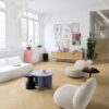 виниловый-ламинат-quick-step-ciro-pure-oak-blush Виниловый ламинат Quick-Step Ciro Pure Oak Blush, уложен на полу и лестнице в гостиной с использованием плинтусов Incizo. Белый диван, белые кресла, небольшие круглые журнальные столики и комод.