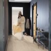 LVT põrand Quick-Step Bloom Sea Breeze Oak Beige paigaldatud koridori põrandale. Naine sisenes tuppa märja vihmavarjuga.