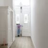 vinyylilattia-quick-step-bloom-botanic-grey Vinyylilattia Quick Step Bloom Botanic Grey asennettuna käytävän lattialle, moderni vaaleanharmaa sävy ja lankkudesign, lapsi lähtee ulos klassisen tyylisestä ovesta.