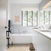Vinyylilattia Quick Step Bloom Sea Breeze Tammi Beige asennettuna kylpyhuoneen lattialle, valkoinen kylpyamme ja valkoiset kylpyhuonekalusteet.
