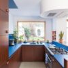 виниловыи-ламинат-quick-step-bloom-sea-breeze-oak-light Виниловый ламинат Quick Step Bloom Sea Breeze Oak Light уложен на полу на кухне, кухонная мебель с синей столешницей и коричневыми фасадами.