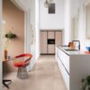 vinyl-floor-tiles-quick-step-oro-coral-rock Vinyl floor tiles Quick-Step Oro Coral Rock installed on kitchen floor. White and beige kitchen furniture. Kitchen table and red stool.