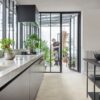 vinyl-tiles-quick-step-illume-oyster-concrete Vinyl tiles Quick-Step Illume Oyster concete installed on a kitchen floor. Kitchen furniture, opened door to summer garden and father and son are watering plants there.