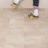 vinylboden-steinoptik-quick-step-oro-coral-rock Vinylboden in Steinoptik Quick Step Oro Coral Rock auf dem Boden verlegt mit Sockelleisten im gleichen Farbton warme korall sandfarbene Steinoptik natürliche Struktur und dezente Farbvariationen Frau auf einem Skateboard