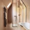 кварц-винил-quick-step-oro-coral-rock Кварц-винил Quick Step Oro Coral Rock уложен на пол в ванной комнате тёплый каменный дизайн в кораллово песочном оттенке естественная фактура и мягкие переходы цвета встроенная ванна чёрная душевая перегородка полотенцесушитель на стене и смесители